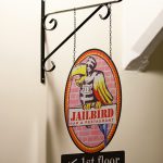 Erikoiskyltti valmistettu mustaksi maalattuun alumiiniin, kuva on tarratuloste, tekstit leikattu tarrakalvosta.