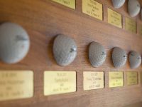 Hole in one -taulu. kaiverretut messinkikilvet upotettu mahonkilevyyn