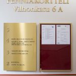 Kerrosopaste messinkiä. Kerrosopasteessa messinkiset kerrosnumerot ja mustat tarratekstit.