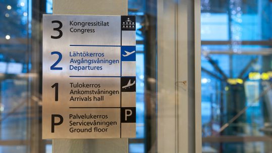 Ruostumattomasta teräksestä kerrosopaste. Opastekyltti kaiverrettu ja maalattu, viimeistelynä hionta