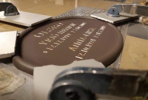 Lisäkaiverrus vanhaan hautalaattaan. Hautakilpeen on kaiverrettu sekä vanha, että uusi teksti.