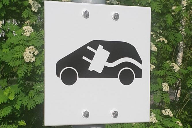 Autopaikkakyltti sähköauton latauspisteestä valkoisella kantatulla alumiinipohjalla, tarrateksti.