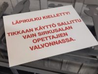 Varoituskilpi valkoista kaiverrusmuovia. Teksti kaiverrettu ja maalattu.